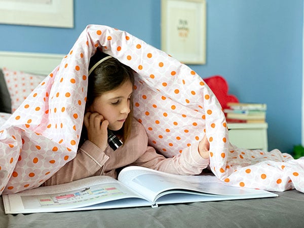 bambina legge libro sotto le coperte